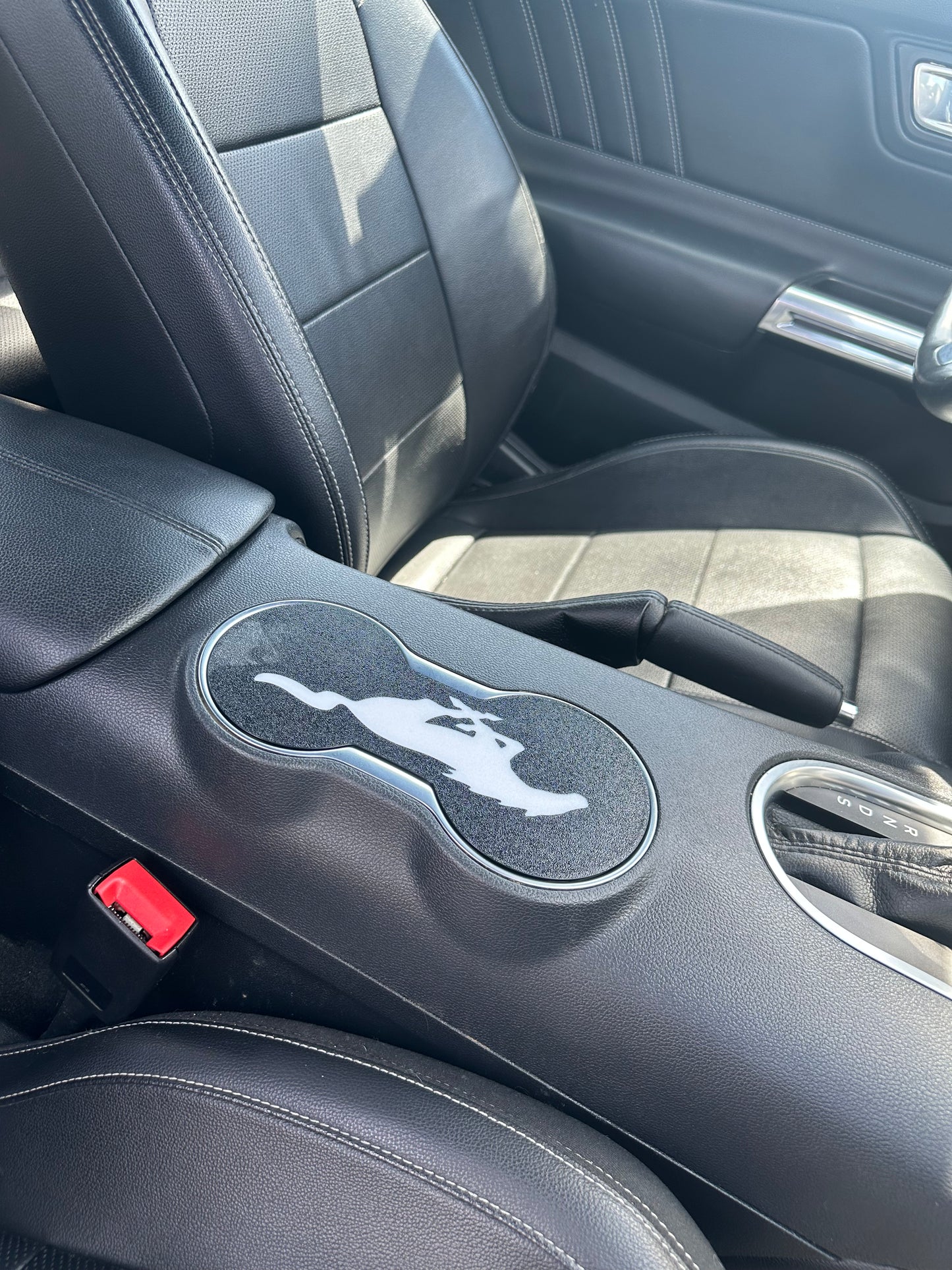 Car interior with a cup holder and logo on a black leather seat.