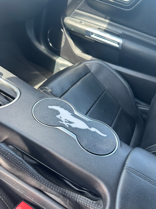 Car interior with a cup holder featuring a logo on a dark gray dashboard.